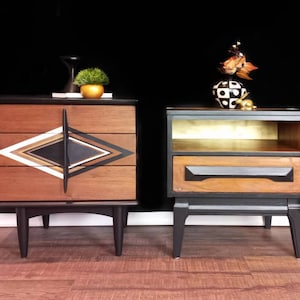 May include: Two mid-century modern nightstands with black painted legs and wood tops. The nightstand on the left has a geometric design on the front. The nightstand on the right has a shelf and a drawer.
