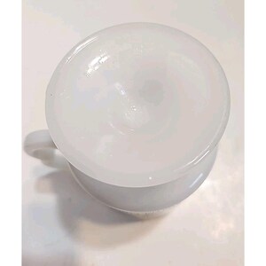 Puede incluir: Vista superior de una taza de cer&aacute;mica blanca con asa. La taza tiene forma redondeada y una superficie lisa y brillante. El interior de la taza tambi&eacute;n es blanco. La taza est&aacute; sobre una superficie blanca.