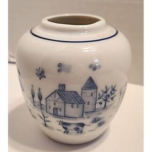 Puede incluir: Una taza de cerámica blanca con asa negra y el texto "But First, Coffee" en negrita negra. La taza se encuentra sobre un fondo borroso, sugiriendo un ambiente acogedor.