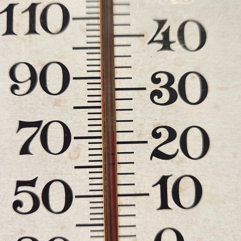 May include: Close-up of a vintage thermometer with black numbers against a cream-colored background. The temperature scale ranges from 0 to 110 degrees Fahrenheit. A red liquid column indicates the current temperature. The thermometer is used to measure temperature.