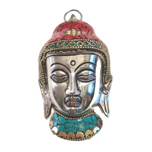 May include: A silver-toned metal pendant shaped like a Buddha head, featuring inlaid red stone fragments on the crown and turquoise stone fragments at the base. The piece includes a small metal loop at the top for hanging and decorative gold-toned accents.