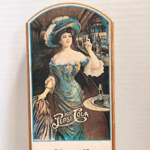 May include: Vintage Pepsi Cola advertisement featuring a woman in a teal dress and feathered hat. The image includes the Pepsi Cola logo and the words "Delicious-Healthful". A bottle and glass of Pepsi are on a small table.