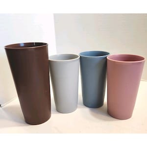May include: Four tall, cylindrical cups in varying colors: brown, light gray, blue-gray, and pink. The cups have a smooth, matte finish and a slightly tapered design, suitable for beverages.