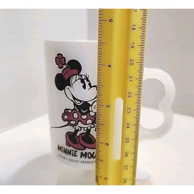 Puede incluir: Taza de cer&aacute;mica blanca con Minnie Mouse. La taza tiene un asa en forma de coraz&oacute;n y una colorida ilustraci&oacute;n de Minnie Mouse con un vestido de lunares. La taza mide aproximadamente 10 cm de alto. El texto "MINNIE MOUSE" y "WALT DISNEY PRODUCT" est&aacute; impreso en la taza.