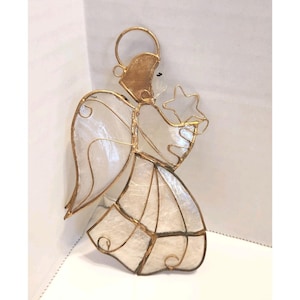 May include: A decorative angel figurine with a gold-colored halo, frame, and star. The angel's wings and dress are white with a textured, translucent appearance. The angel is holding a star.