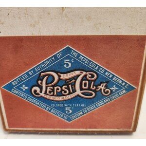 May include: Vintage Pepsi-Cola advertisement featuring a diamond-shaped logo with the Pepsi-Cola name in a stylized script. The logo is set against a red background, with text indicating the drink is "Delicious, Healthful" and costs 5 cents.