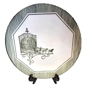 May include: A decorative plate with a black and white design. The plate features an octagonal center with a black and white illustration of a building and horse-drawn carriage. The outer rim has a textured, striped pattern.