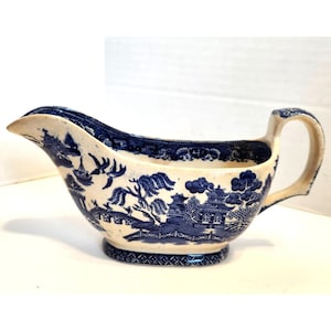 Puede incluir: Salsera crema con un patrón azul Willow. La salsera tiene un pico, un asa y una base decorativa. El diseño azul y blanco representa un paisaje con pagodas, árboles y pájaros. Una pieza clásica para servir salsas.