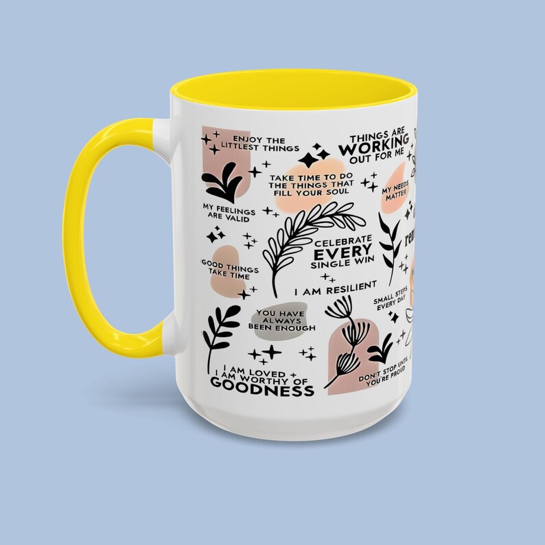 Puede incluir: Taza de cer&aacute;mica blanca con interior y asa amarillos. La taza est&aacute; decorada con frases inspiradoras e ilustraciones bot&aacute;nicas en negro y melocot&oacute;n. El texto incluye "Disfruta de las peque&ntilde;as cosas" y "Celebra cada victoria".