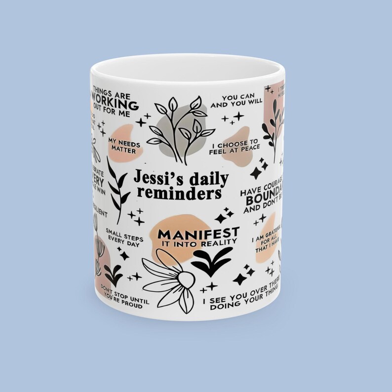 Puede incluir: Taza de cer&aacute;mica blanca con el texto "Jessi's daily reminders" y frases inspiradoras en negro. La taza presenta dise&ntilde;os florales y geom&eacute;tricos en negro y melocot&oacute;n.