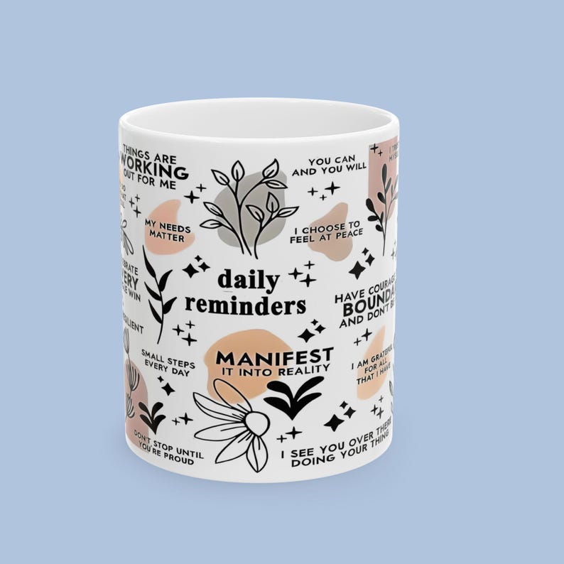 Puede incluir: Taza de cer&aacute;mica blanca con las palabras "daily reminders" y frases inspiradoras en negro, con dise&ntilde;os florales y geom&eacute;tricos en negro y melocot&oacute;n. La taza es de tama&ntilde;o est&aacute;ndar.