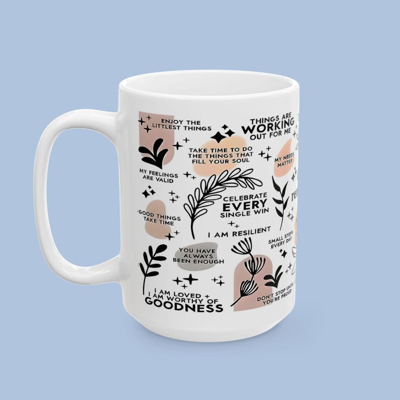 Puede incluir: Taza de cer&aacute;mica blanca con un asa grande, decorada con frases inspiradoras e ilustraciones bot&aacute;nicas en negro y melocot&oacute;n. La taza presenta textos como "Celebra cada victoria" y "Soy resiliente".