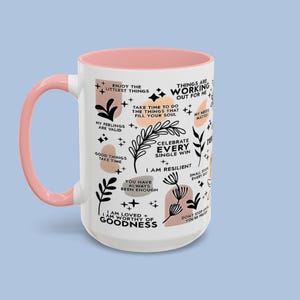 Puede incluir: Taza de cer&aacute;mica blanca con asa e interior rosa. La taza est&aacute; decorada con frases inspiradoras e ilustraciones bot&aacute;nicas en negro y melocot&oacute;n. Las frases incluyen "Disfruta de las cosas m&aacute;s peque&ntilde;as" y "Celebra cada victoria."
