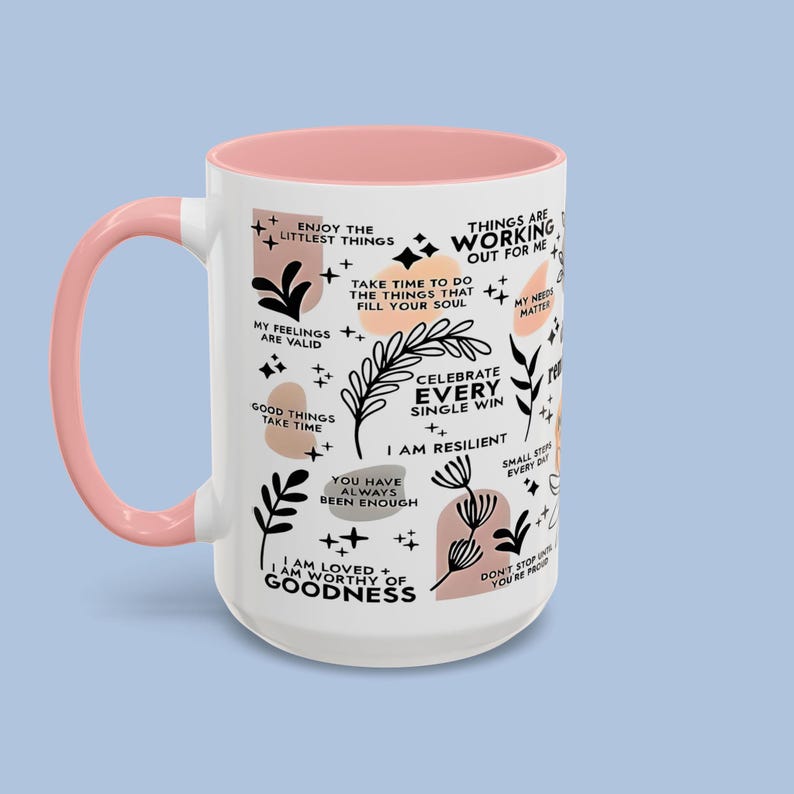 Puede incluir: Taza de cer&aacute;mica blanca con asa e interior rosa. La taza est&aacute; decorada con frases inspiradoras e ilustraciones bot&aacute;nicas en negro y melocot&oacute;n. Las frases incluyen "Disfruta de las cosas m&aacute;s peque&ntilde;as" y "Celebra cada victoria."