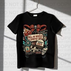Może przedstawiać: Czarny t-shirt z kolorową grafiką z napisem "HELL ON WHEELS & COUNTRY SOUL." Projekt zawiera czaszkę, kokardę, kapelusz kowbojski i inne elementy w stylu western. Koszulka wisi na białym wieszaku.