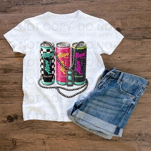 Pode incluir: Camiseta branca com um gr&aacute;fico de tr&ecirc;s latas de bebida energ&eacute;tica Alani em designs xadrez preto e branco, rosa e estampa de leopardo. Um colar com pingente turquesa e shorts jeans completam o look.