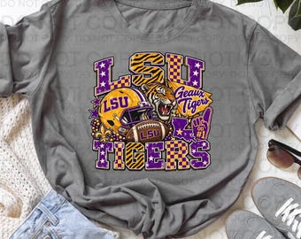 Könnte beinhalten: Ein graues T-Shirt mit einem Grafikdesign, das den Text LSU TIGERS, einen gelben Football-Helm, ein Tigergesicht, einen Football, eine Fleur-de-Lis, eine Karte von Louisiana und einen Schaumstofffinger in Violett, Gelb und Weiß zeigt.