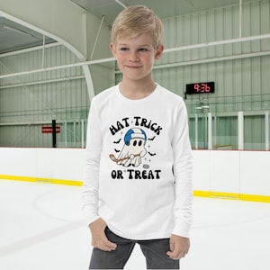 May include: White long-sleeve shirt with a ghost wearing a hockey helmet and holding a hockey stick. The shirt has the text "Hat Trick or Treat" printed on it.