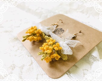 May include: A pair of crocheted flower earrings with yellow and green flowers and white lace bows. The earrings are on a brown card.