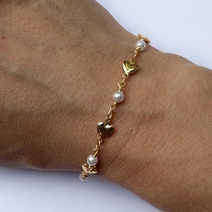 May include: A gold chain bracelet with small heart charms and white pearl beads.