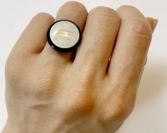 May include: A white and black ring with a round, textured, white stone set in a black metal band.