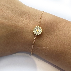 May include: A delicate gold chain bracelet with a white daisy charm featuring a yellow centre.