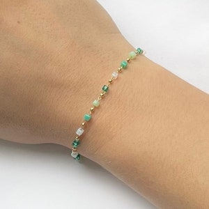 May include: A delicate gold chain bracelet with green and white square beads.