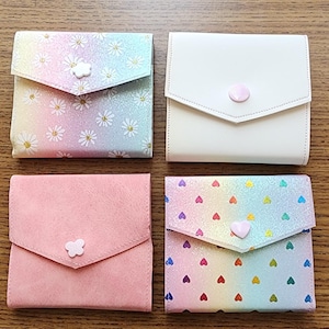 May include: Four small, colorful, fabric pouches with different patterns and designs. Each pouch has a flap with a button closure. The pouches are arranged in two rows of two on a wooden surface.