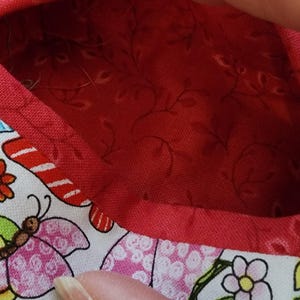 Op de afbeelding: Een kleine, open container met een rode binnenkant en een witte buitenkant met kleurrijke vlinders en bloemen. De container heeft een rode rand.