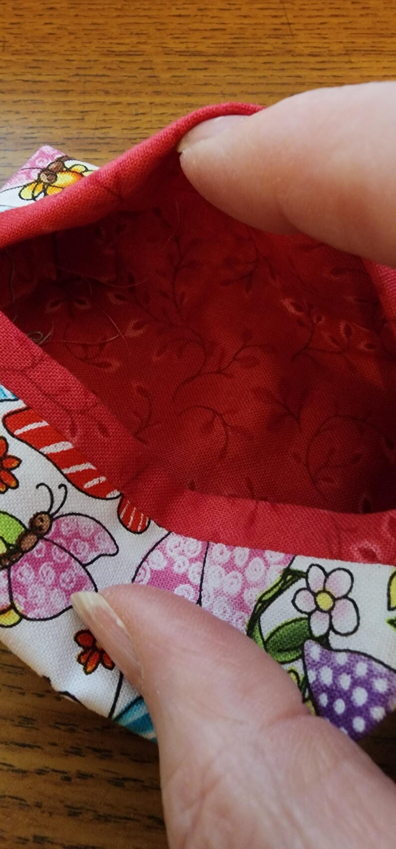Op de afbeelding: Een kleine, open container met een rode binnenkant en een witte buitenkant met kleurrijke vlinders en bloemen. De container heeft een rode rand.