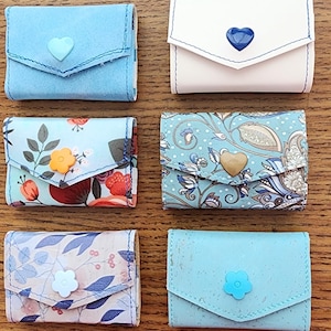 May include: Six small blue and white patterned wallets with different designs. Each wallet has a flap closure and a heart or flower shaped button.