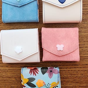 May include: Five small pouches with different designs. The pouches are made of fabric and have a flap closure. The pouches are decorated with different colored buttons in the shape of hearts, butterflies, and flowers.