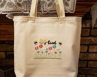 May include: A beige canvas tote bag with the embroidered text "Bee kind" and a row of colorful flowers and bees.