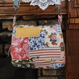 May include: A patchwork fabric crossbody bag with a floral print and a yellow and white striped patch. The bag has a flap closure and a silver metal clasp.