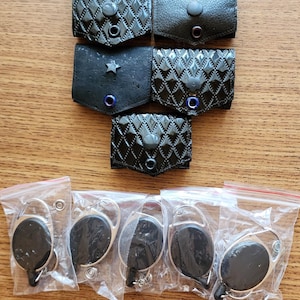 May include: Six black leather keychains with a star, a circle, and a diamond pattern. Five black retractable badge holders in clear plastic bags.