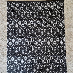 May include: Black and white fabric with a geometric pattern of circles, diamonds, and zigzags. The fabric is folded in thirds.