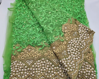 Puede incluir: Tela bordada verde brillante con un patrón floral y adornos dorados. La tela tiene un diseño detallado con pequeñas perlas blancas redondas y lentejuelas doradas. Adecuada para ropa o fines decorativos.