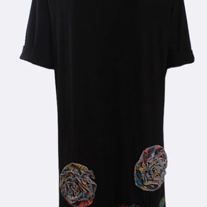 May include: Black, short-sleeved dress with a scoop neck. The dress has two large, colourful floral appliqués and several leaf-shaped appliqués near the hem. The text "LOVE MY FASHIONS" is printed on the neckline.