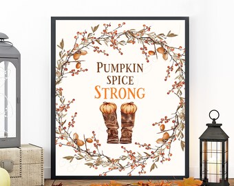 May include: A white printable art print with a fall-themed design. The print features a wreath of brown branches with red berries and a pair of brown boots with orange tops. The text "Pumpkin Spice Strong" is written in orange letters.