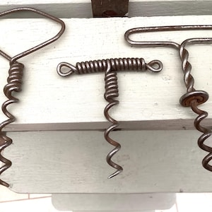 May include: Three vintage metal corkscrews. The corkscrews feature distinct handle designs: a diamond, a T-shape, and a twisted handle. Each corkscrew has a spiral worm for removing corks from bottles. The metal has a rustic, aged appearance.