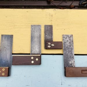 Könnte beinhalten: Eine Sammlung antiker Holzbearbeitungswinkel mit Holzgriffen und Metallklingen. Die Winkel sind auf einer gelb-blauen Oberfläche angeordnet und zeigen ihr gealtertes Aussehen und ihre Handwerkskunst. Die Klingen weisen Gebrauchsspuren auf.