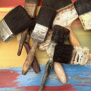 Könnte beinhalten: Eine Sammlung gebrauchter Farbpinsel mit dunklen Borsten und abgenutzten Holz- oder Metallgriffen. Die Pinsel haben Metallzwingen, die teilweise Spuren von getrockneter Farbe und Abnutzung aufweisen. Die Pinsel sind in einer Gruppe angeordnet.