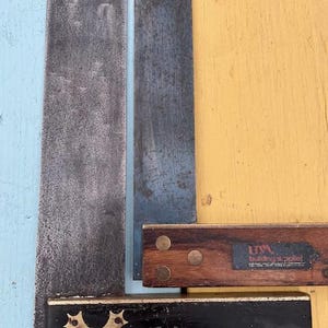 May include: A collection of antique woodworking tools. The image shows a large metal straight edge, a smaller blue metal piece, and two wooden squares. One square is black with a brass design, the other is brown with brass rivets.