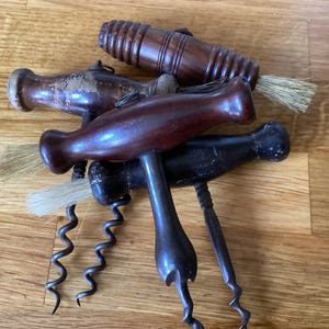 May include: Several antique corkscrews with wooden handles and metal spirals. The corkscrews are in shades of brown and black, with some showing signs of wear. Some have small brushes attached.