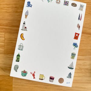 May include: White notepad with watercolor illustrations of summer and beach-themed items, including a lobster, ice cream cone, and sailboat. The notepad is surrounded by colorful drawings and is on a wooden surface.