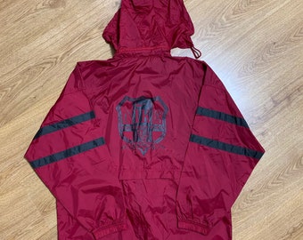 Puede incluir: Una chaqueta cortavientos de color granate con rayas negras en las mangas. La chaqueta tiene capucha y cierre de cremallera. La parte posterior de la chaqueta presenta un logotipo en blanco y negro que dice "UNITY FOUR CHAMPS 1997".