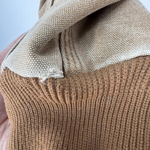 Puede incluir: Primer plano de una tela beige con textura tejida, superpuesta a un material de punto marr&oacute;n acanalado. Las telas est&aacute;n dobladas, revelando las diferentes texturas y colores. La imagen resalta el contraste entre el material tejido liso y el punto texturizado.