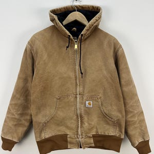 Puede incluir: Chaqueta con capucha marr&oacute;n con cremallera, bolsillo delantero y dobladillo y pu&ntilde;os acanalados marrones. La chaqueta tiene un forro interior negro y un peque&ntilde;o parche con el logo en la parte delantera.