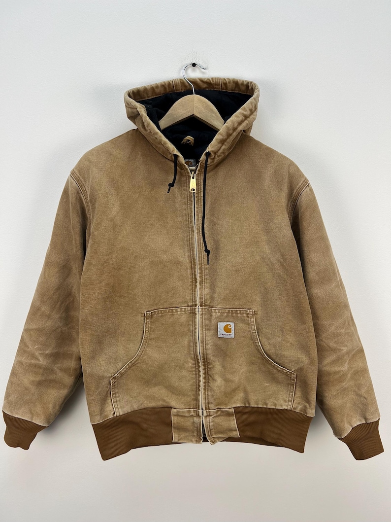 Puede incluir: Chaqueta con capucha marr&oacute;n con cremallera, bolsillo delantero y dobladillo y pu&ntilde;os acanalados marrones. La chaqueta tiene un forro interior negro y un peque&ntilde;o parche con el logo en la parte delantera.