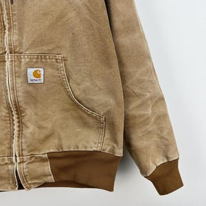 Puede incluir: Chaqueta con capucha Carhartt de color marr&oacute;n claro con cremallera frontal, bolsillo tipo canguro y pu&ntilde;os y dobladillo acanalados. El logotipo de Carhartt est&aacute; en un peque&ntilde;o parche cuadrado en el bolsillo delantero. Tejido resistente.